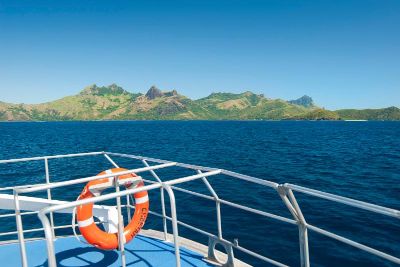 Life ring on the railing of a boat cruising out at sea with Way island in Fiji in the background