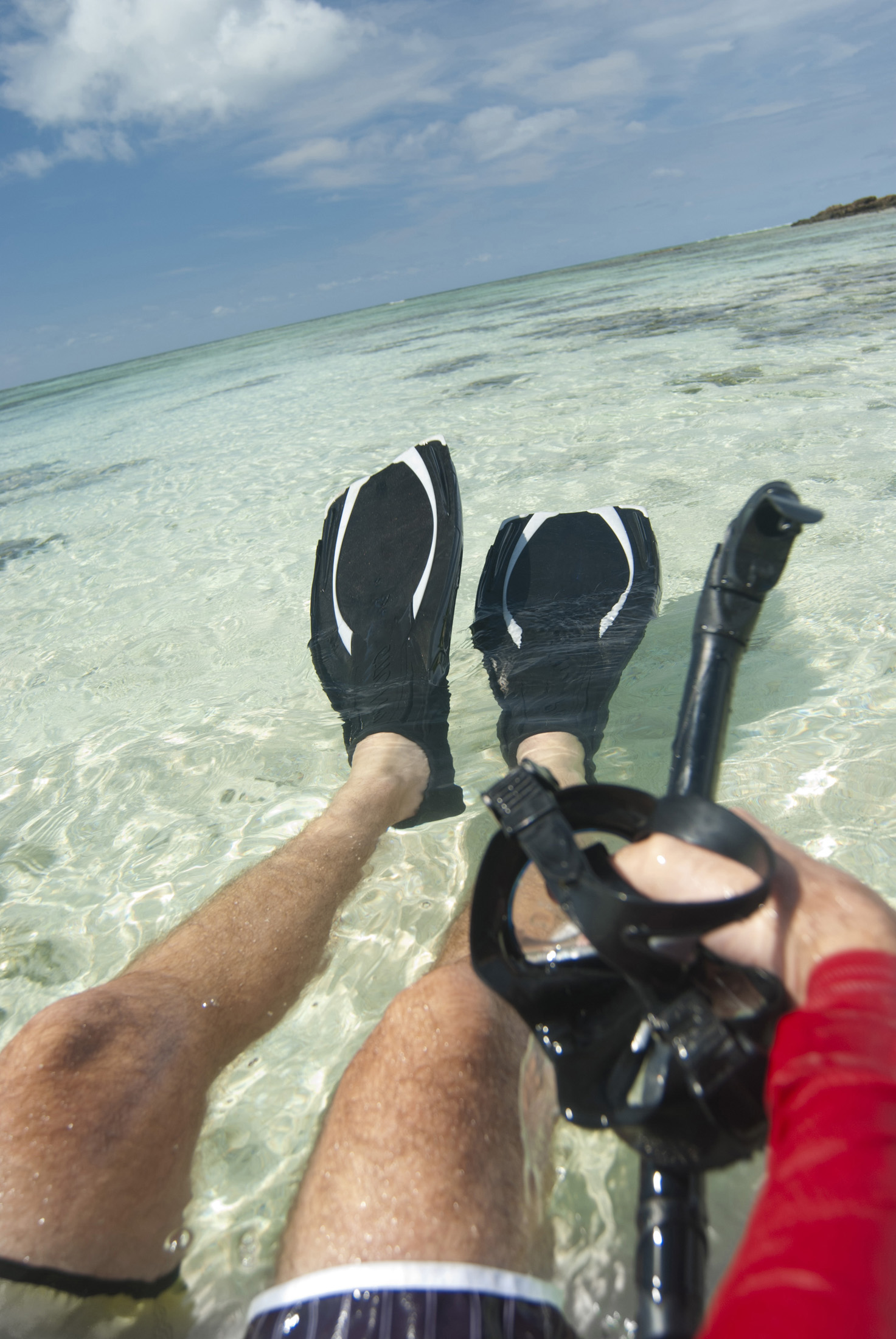 an image of Cropped view of a man floating in crystal clear tropical water wearing flippers with a snork and goggles in his hand