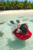 Man snorkeling in shallow crystal clear water off a tropical island beach floating on his back clearing his goggles