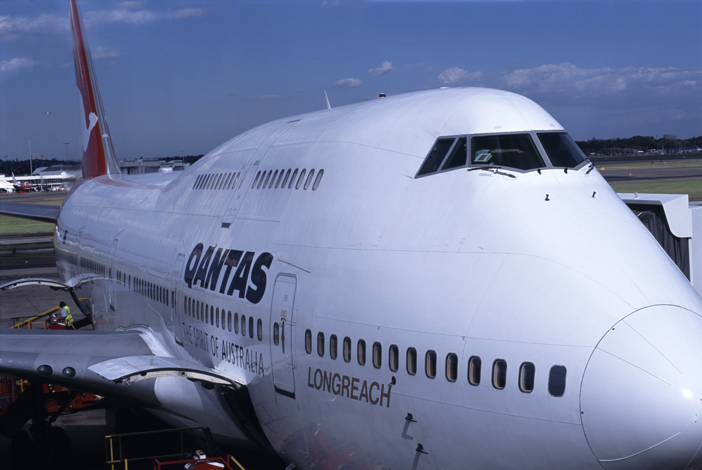 an image of Qantas passenger airplane on the apron at an airport refueling and embarking passengers for an international flight, close up view of the front and pilots cockpit
