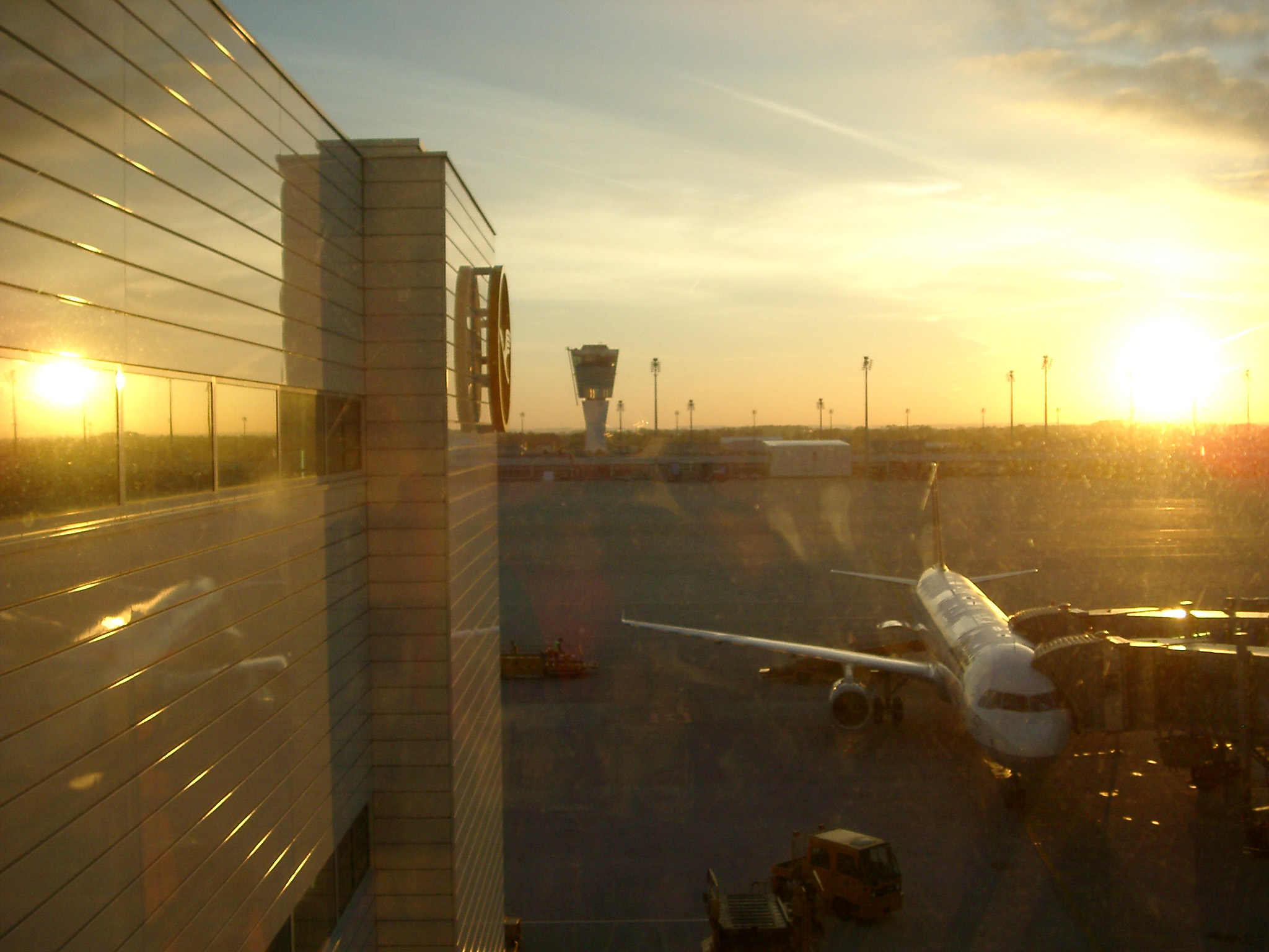 an image of Airport at sunset with a view along the exterior of the building onto the apron and an aircraft loading for departure