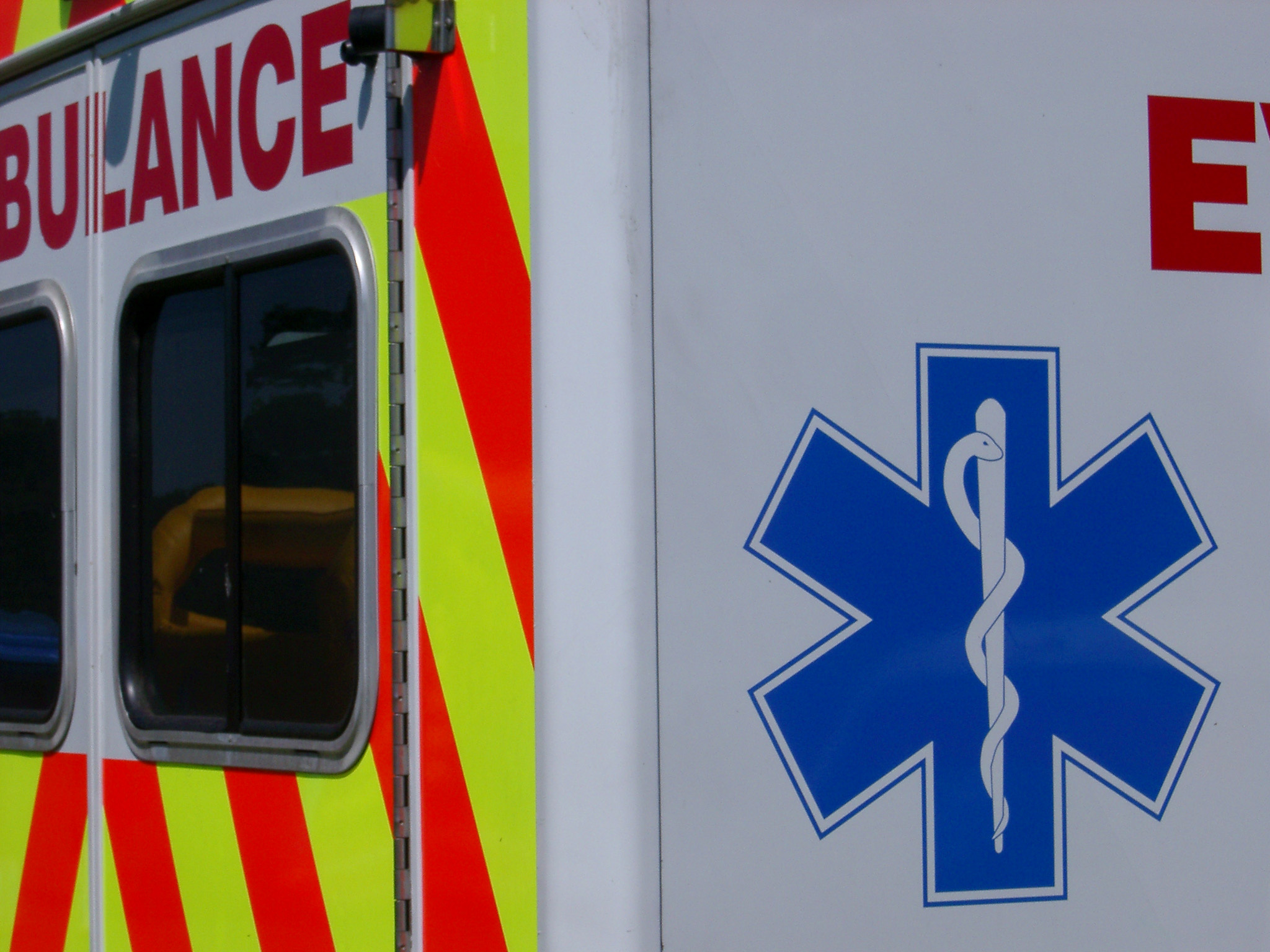 an image of Ambulance showing the snake and staff symbol of the emergency medical service with a portion of the rear door and red and yellow neon chevron visible