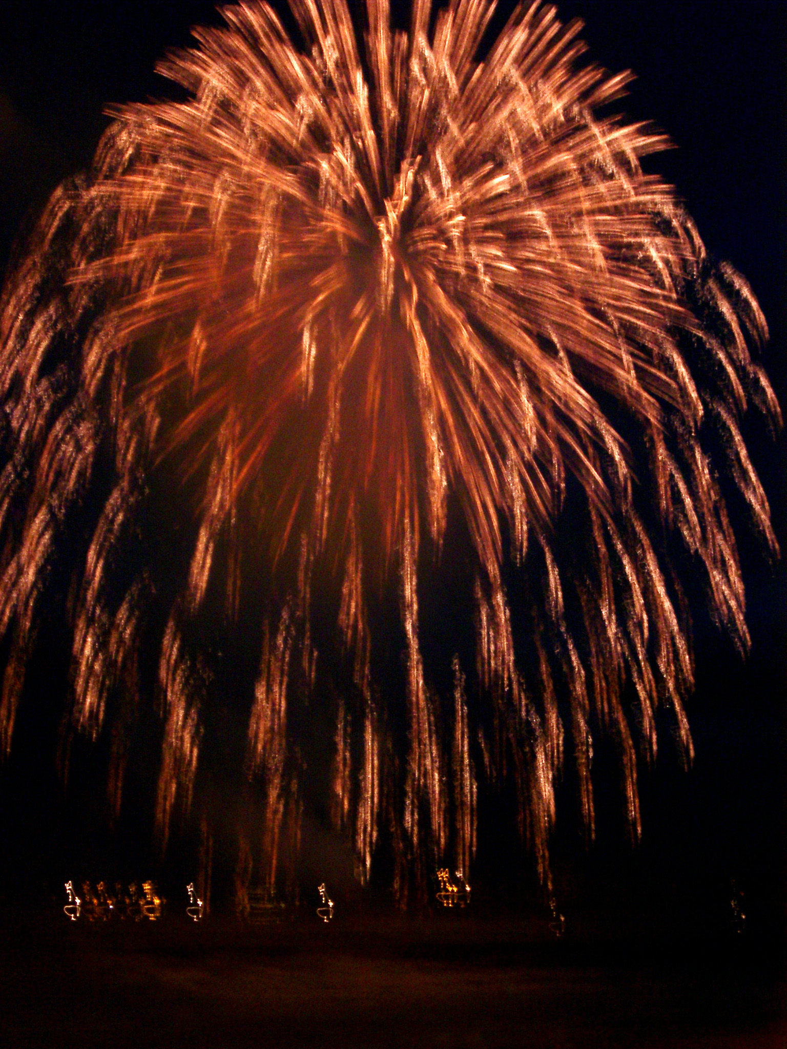 an image of Colorful red orange firework display with a rocket exploding in a ball of fiery sparks and trails in a night sky during a festival, carnival or celebration
