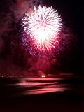 Long Exposure of Pink Fireworks Exploding in Sky Above Water at Night