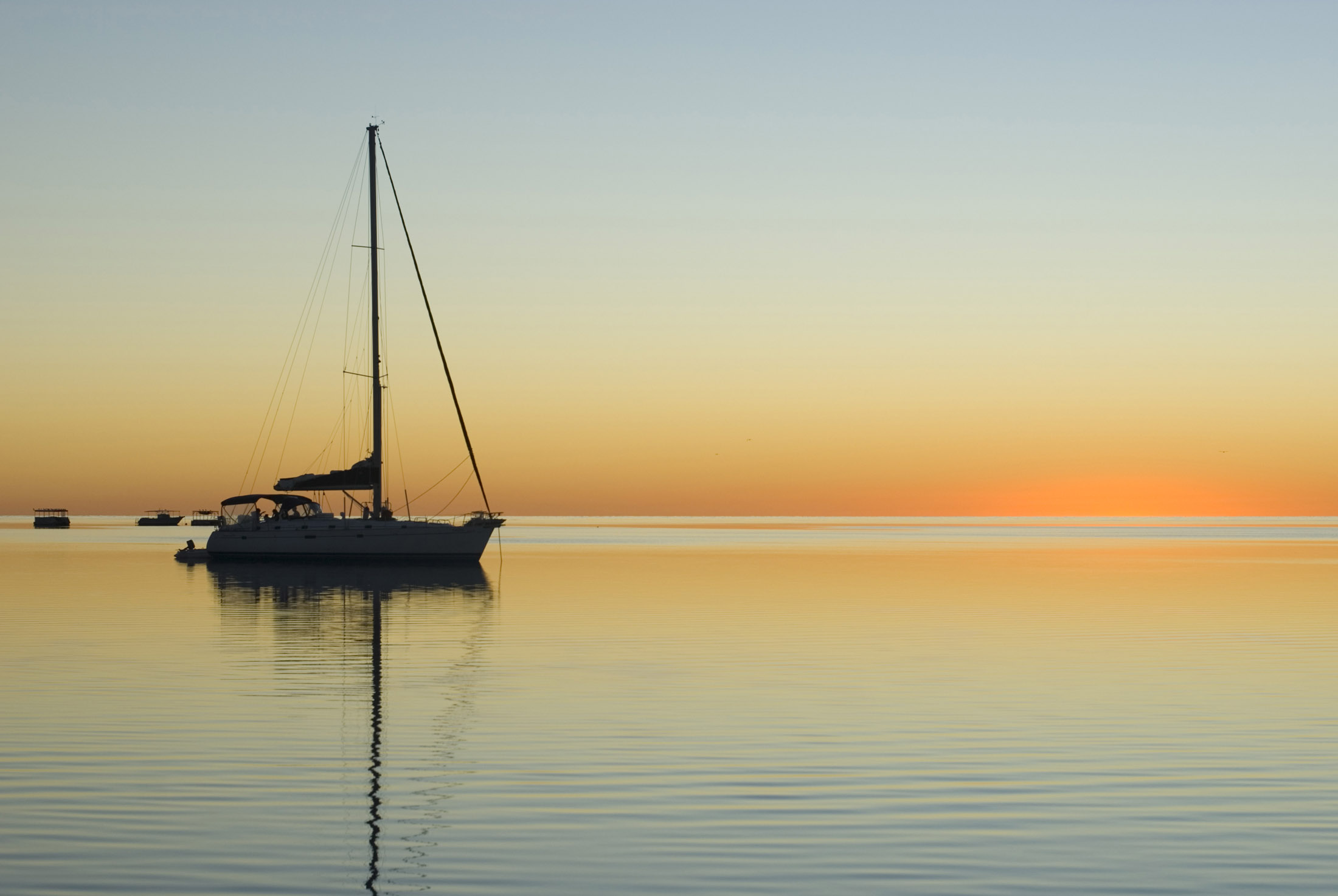 an image of sunset over calm tropical waters with the silhouette of a sailing yacht
