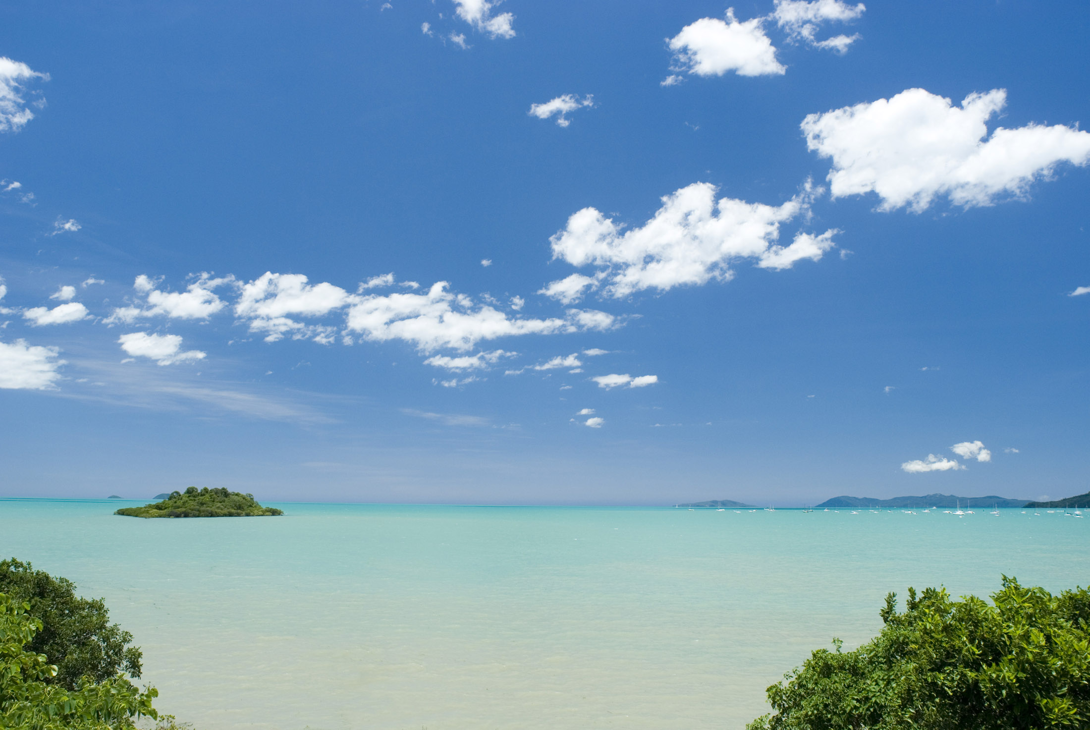 an image of an oceanscape of crystal blue tropical waters with bluy sky and fliuffy clouds