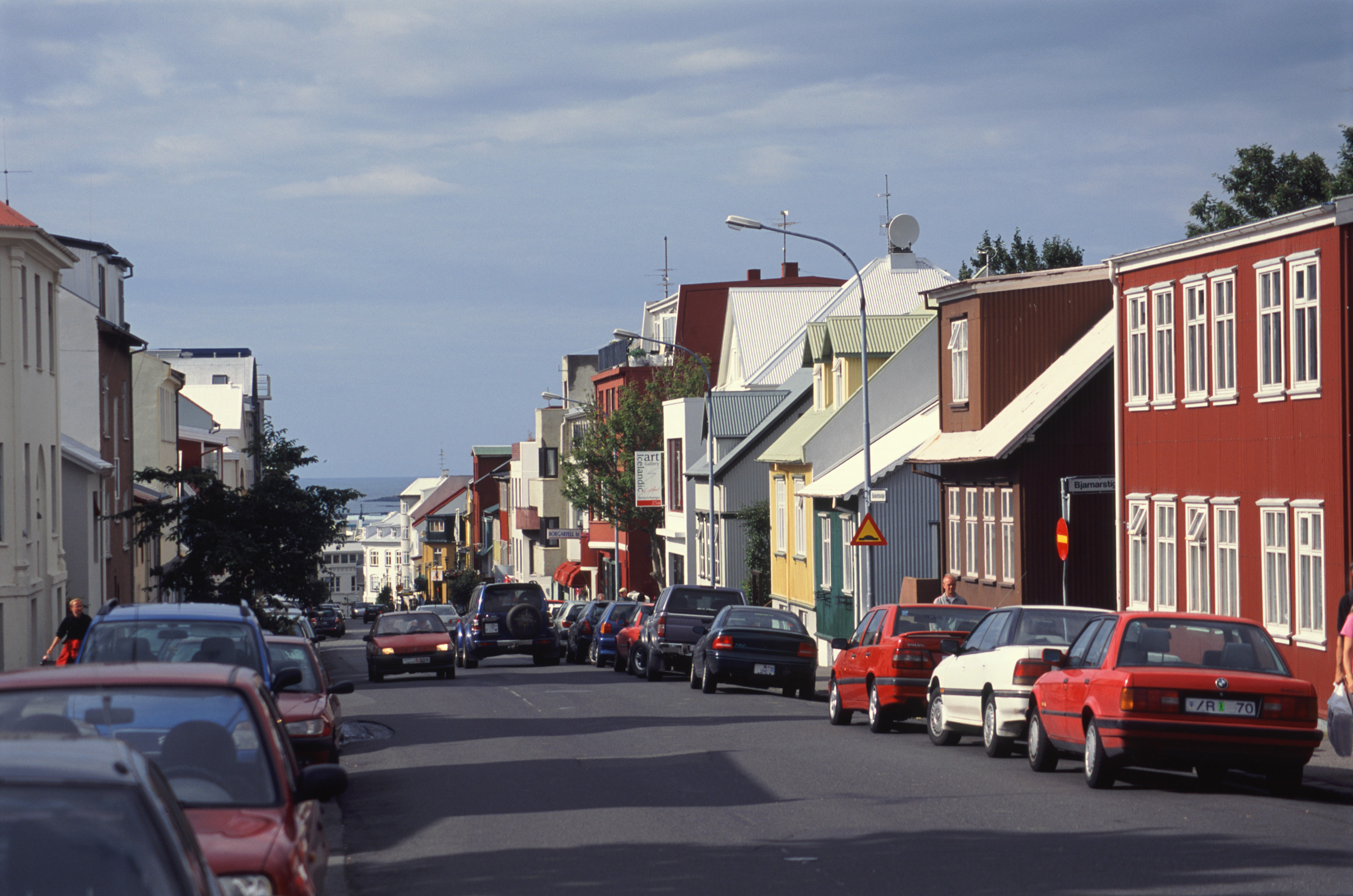 an image of Street scene in Reykjavik, Iceland with traditional architecture and rows of parked cars on a sunny day