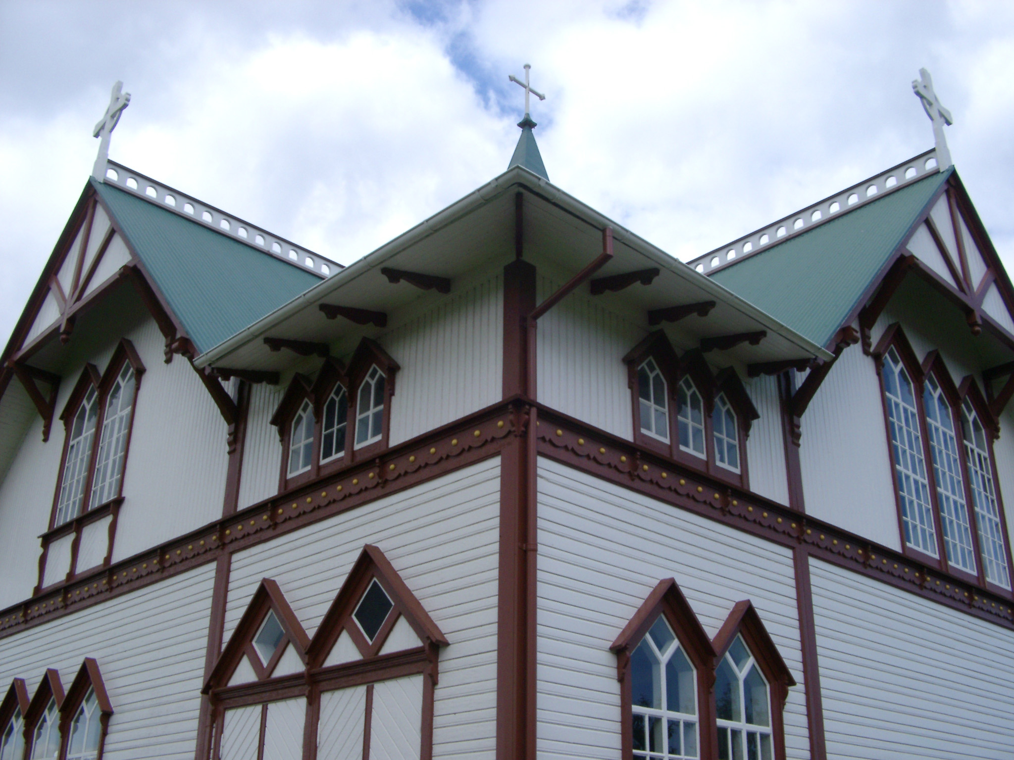 an image of Exterior of the church in Husavik in Iceland with ornate windows and a roof adorned with crosses against a cloudy blue sky