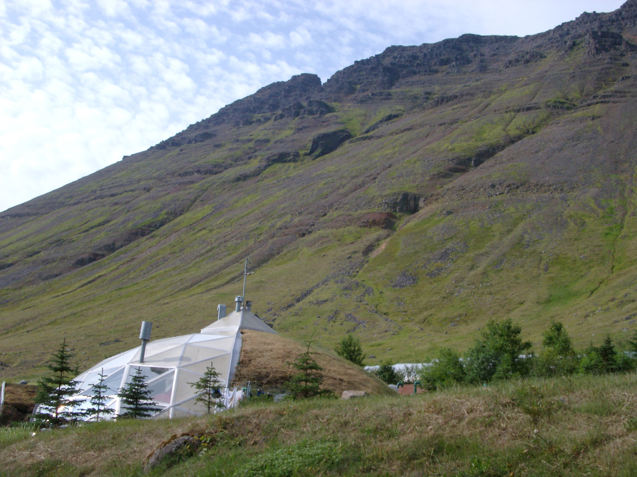 an image of Environmentally friendly biodome, or dome house in Isafjordur in Iceland partially covered in turf built at the foot of a volcanic mountain