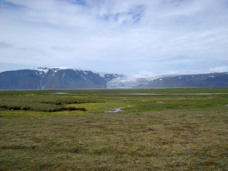 View over meltwater lakes and streams ringed with green grass to a distant volcanic mountain glacier in Iceland in a scenic landscape