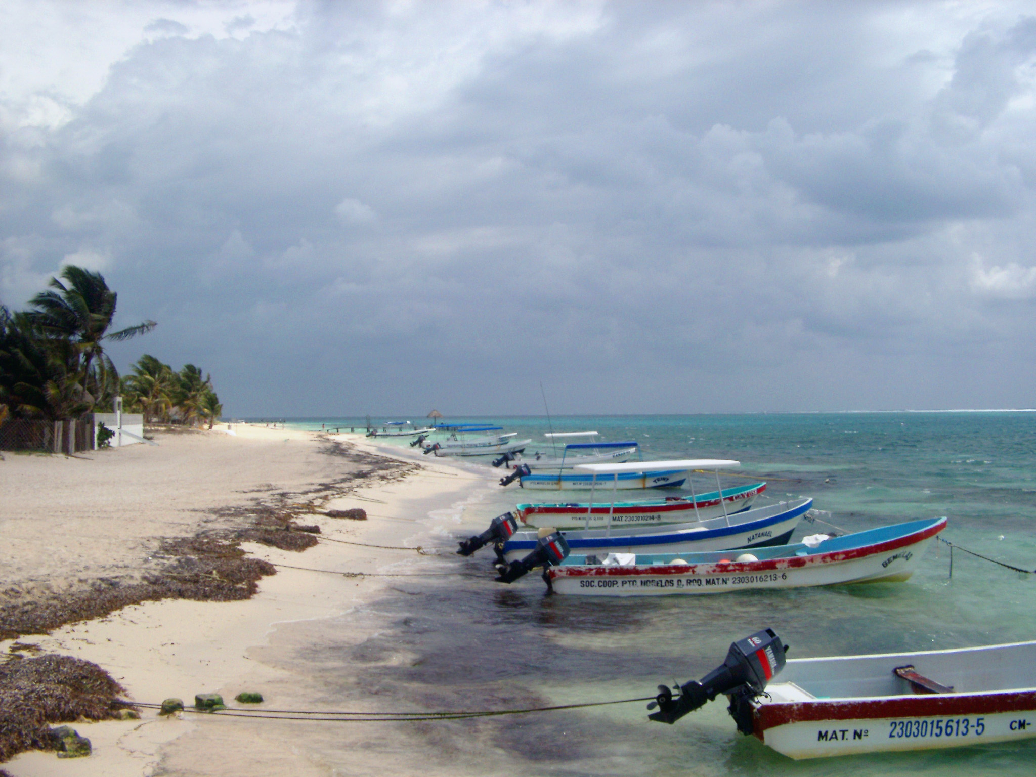 an image of Small motorboats moored to the shoreline in Mexico with their bows pointing out to sea on a golden tropical beach under a cloudy summer sky