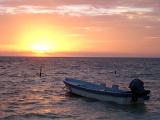 Colorful Caribbean sunset with a glowing orange sun dipping below the ocean and a moored wooden motorboat in the foreground