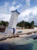 Leaning tower on a beach in Mexico whose foundations have been eroded by the tides in front of a typical small Mexican village