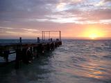 Wooden jetty lined with a row of old tyres for mooring at sunrise with the glowing orb of the sun appearing above the ocean, Mexico