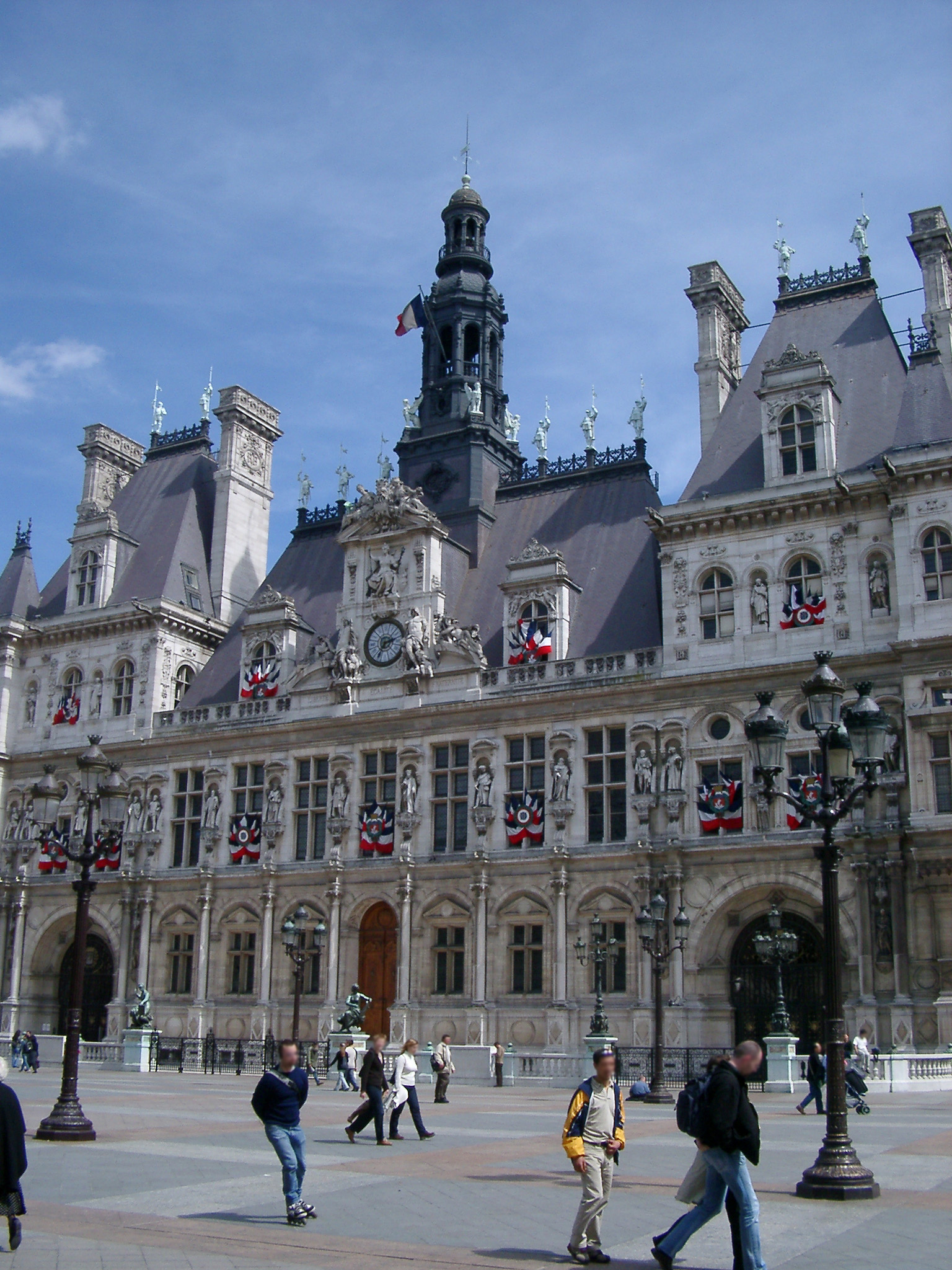 an image of Exterior view of the ornate historical stone facade of the Paris City Hall or Hotel de Ville with pedestrians in the foreground