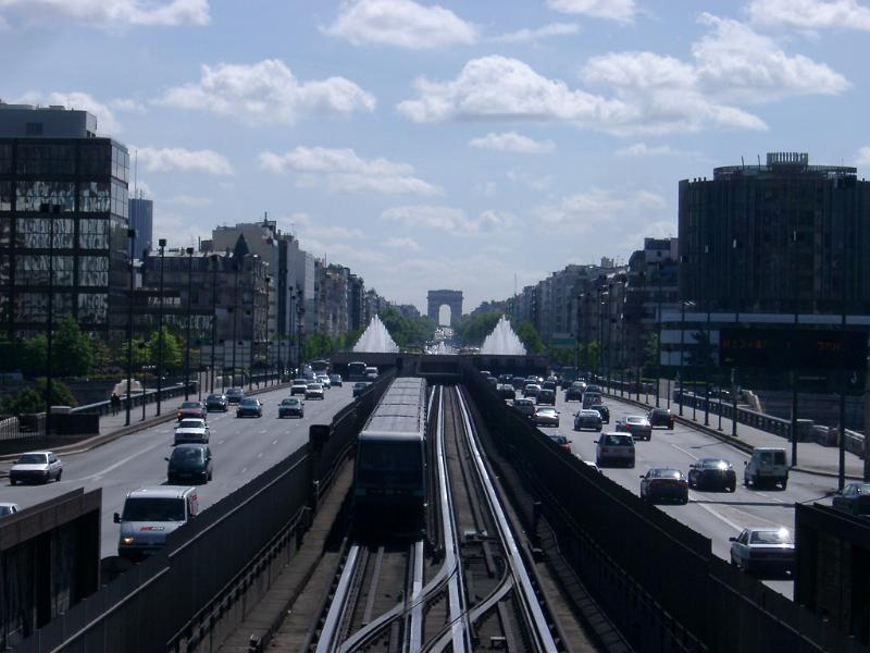 Assorted Vehicles at Busy City Metro Lines with Tall Concrete Buildings on Sides. Isolated on Light Blue Sky Background.