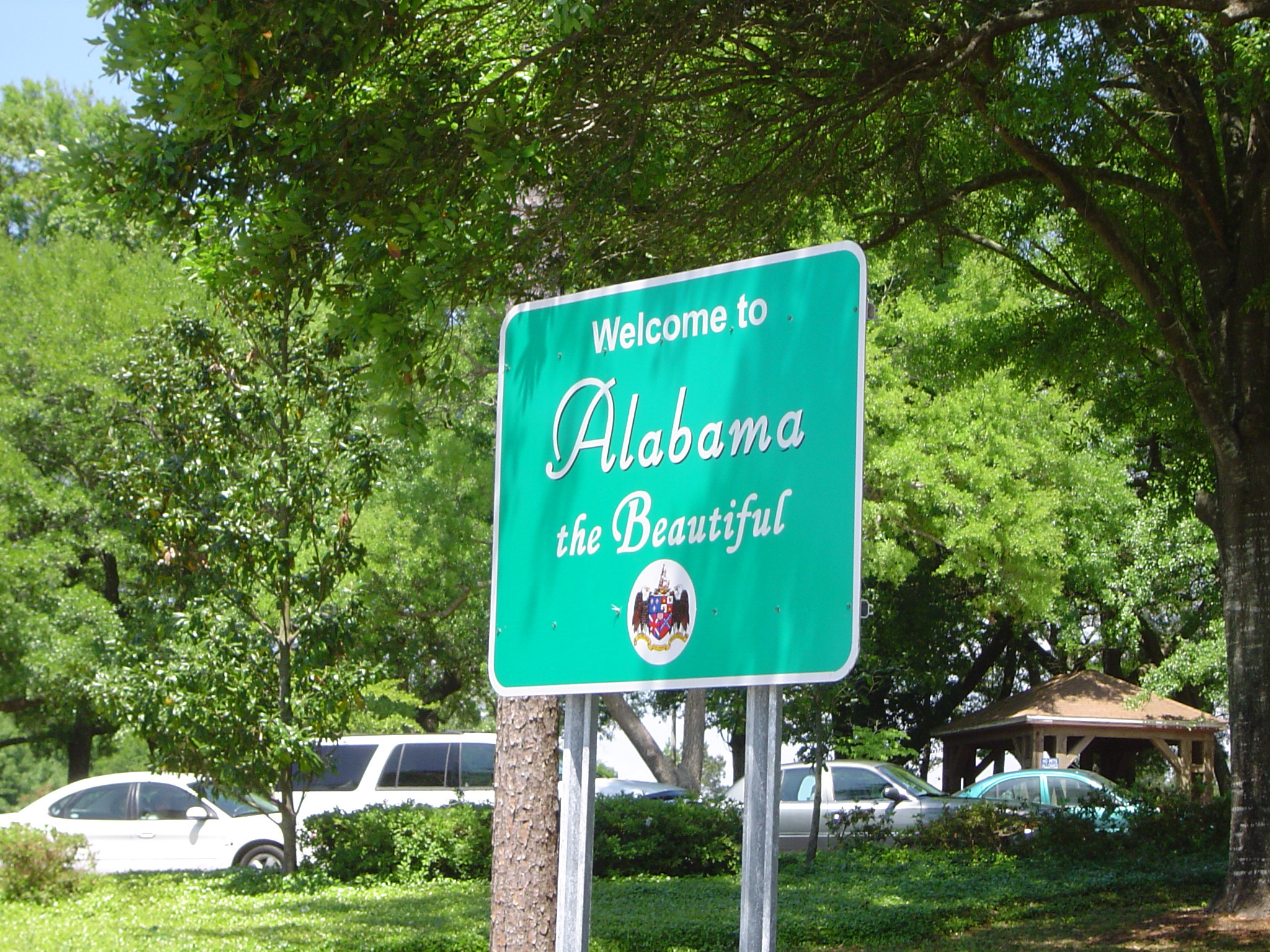 an image of Alabama welcome road sign at the side of a leafy green street conceptual of a road trip vacation driving around the USA