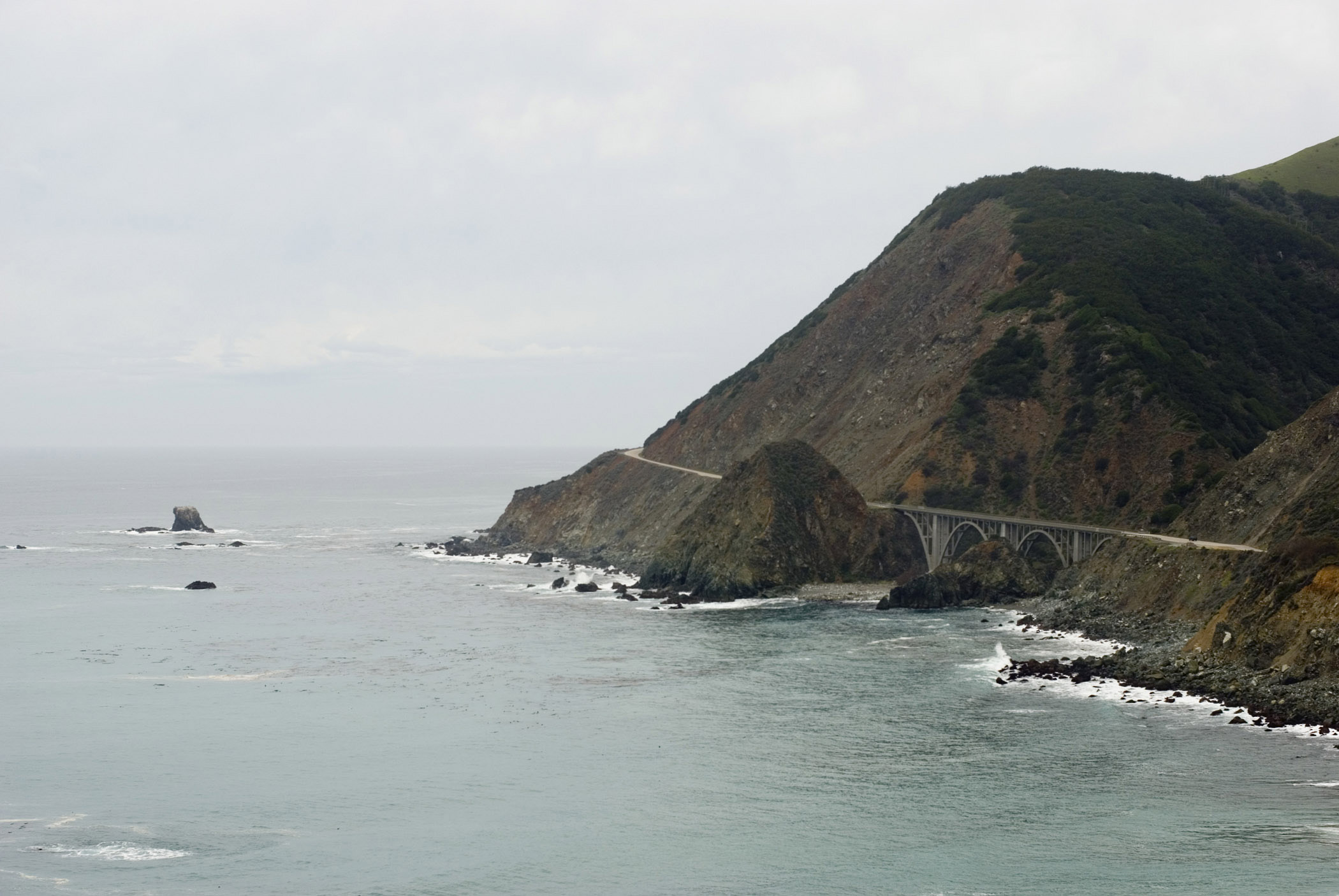 an image of Rocky Big Creek Bridge at Beautiful Big Sur Coast Portrait. Isolated on Lighter Gray Sky Background.
