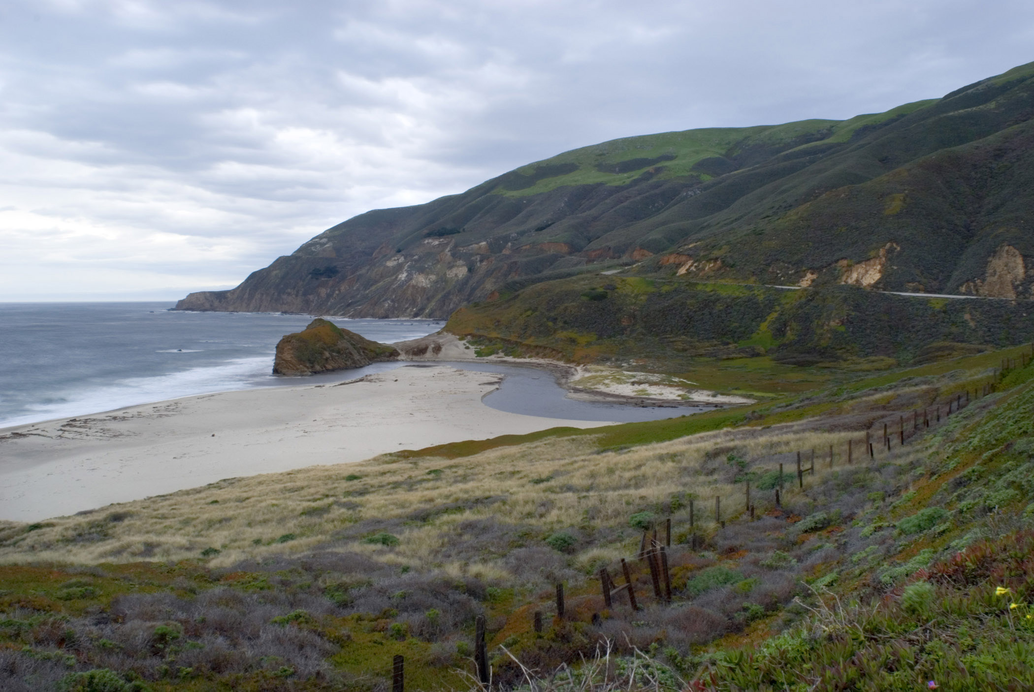 an image of Beautiful Big Sur Coast Seascape in Extensive View. Captured with Relaxing Sea, Grassy Campground and Huge Mountain. Isolated on Light Gray Sky Background.