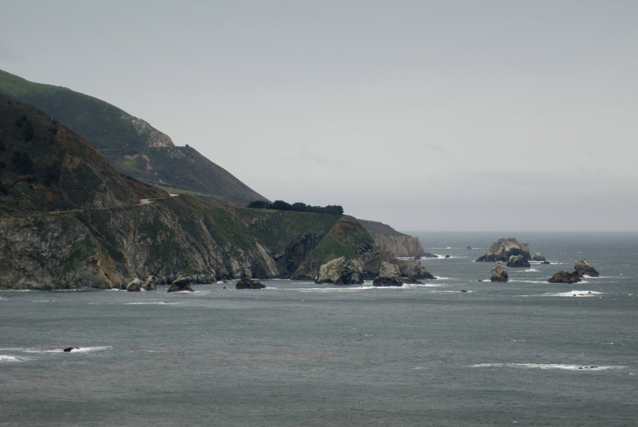 an image of Big Sur coast, California on a grey overcast rainy day with a rocky headland jutting out into a calm ocean