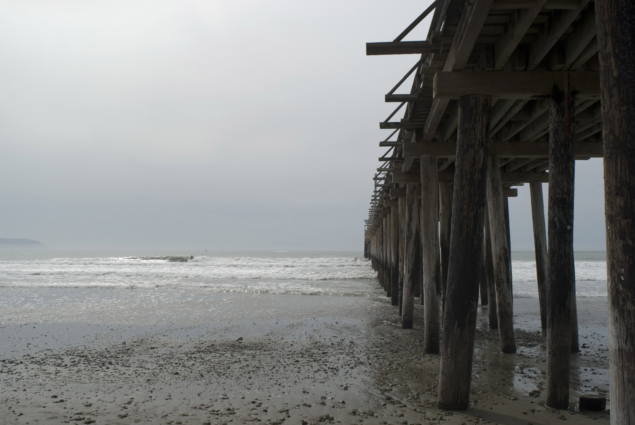 an image of View Underneath the Wooden Columns at Cayucos Pier. Isolated on Light Gray Sky Background.
