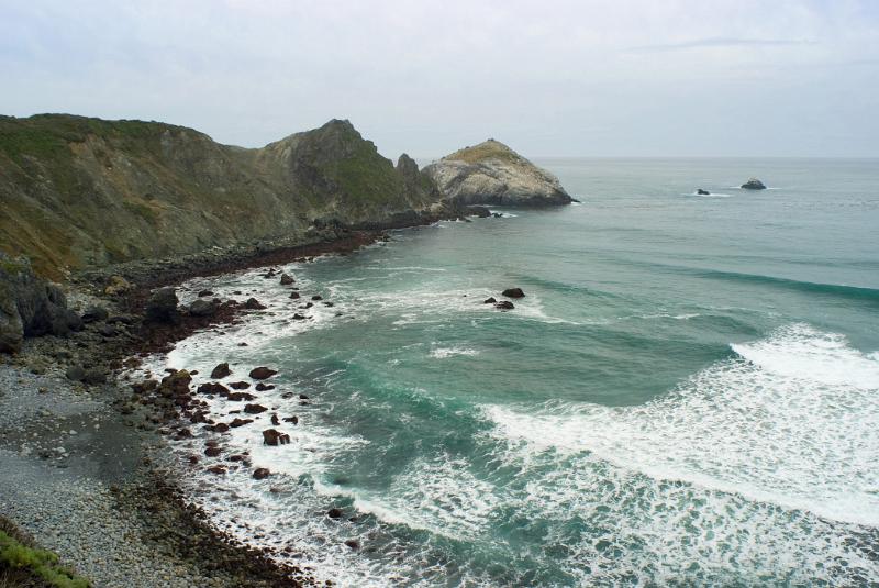 Beautiful Big Sur Coast Seascape in Aerial View. Captured with Grassy Hills in Front on Lighter Blue Gray Sky Background.