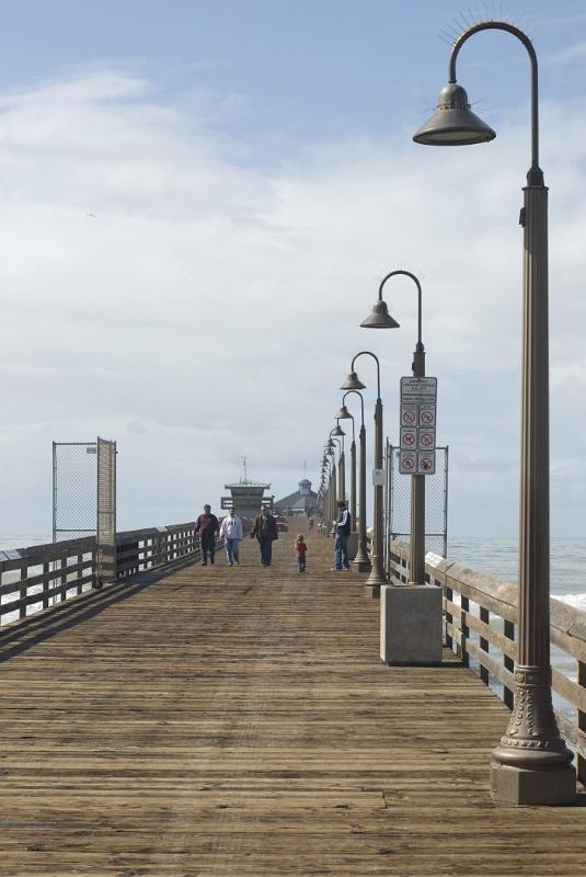 Tourists Walking on Vintage Pathway with Long Stand Lights Heading to Imperial Beach Restaurant. Isolated on White and Lighter Blue Sky Background.