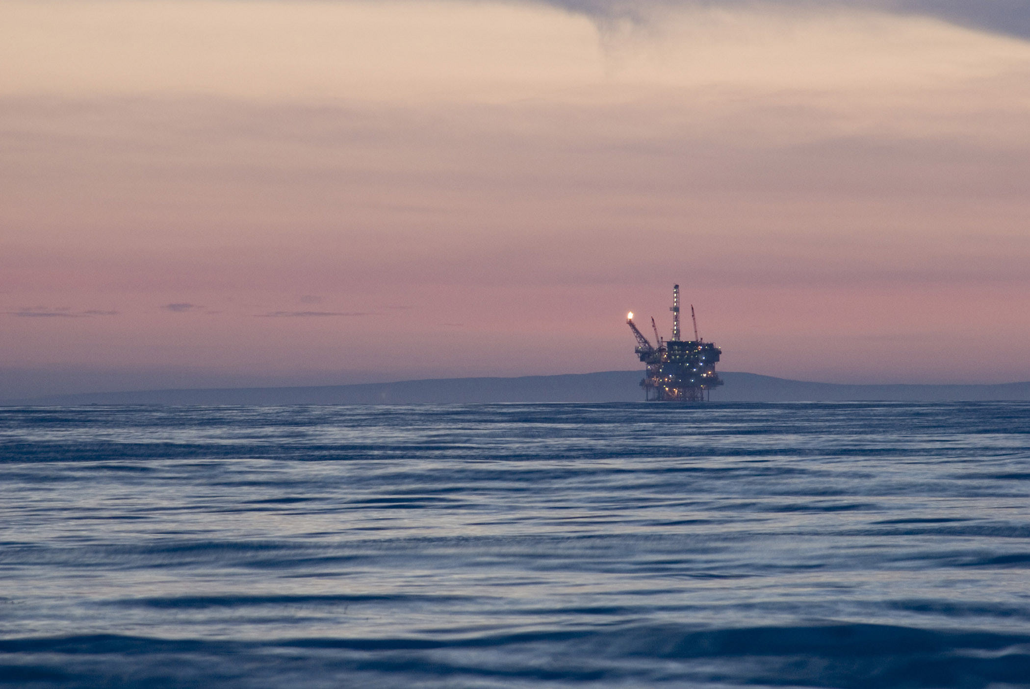 an image of Offshore oil rig in the Gulf of Mexico off California at dusk with a colorful pink sky above a calm ocean