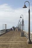 Tourists Walking on Vintage Pathway with Long Stand Lights Heading to Imperial Beach Restaurant. Isolated on White and Lighter Blue Sky Background.