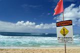 Rip Current warning notice forbidding swimming on a beach or you could be swept out to sea and drown, with copyspace over a tropical ocean and golden sand