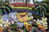 Colorful Helemano Plantation sign on a pineapple plantation visitor center in Hawaii with palm trees, frangipani and hibiscus flowers and peoples faces