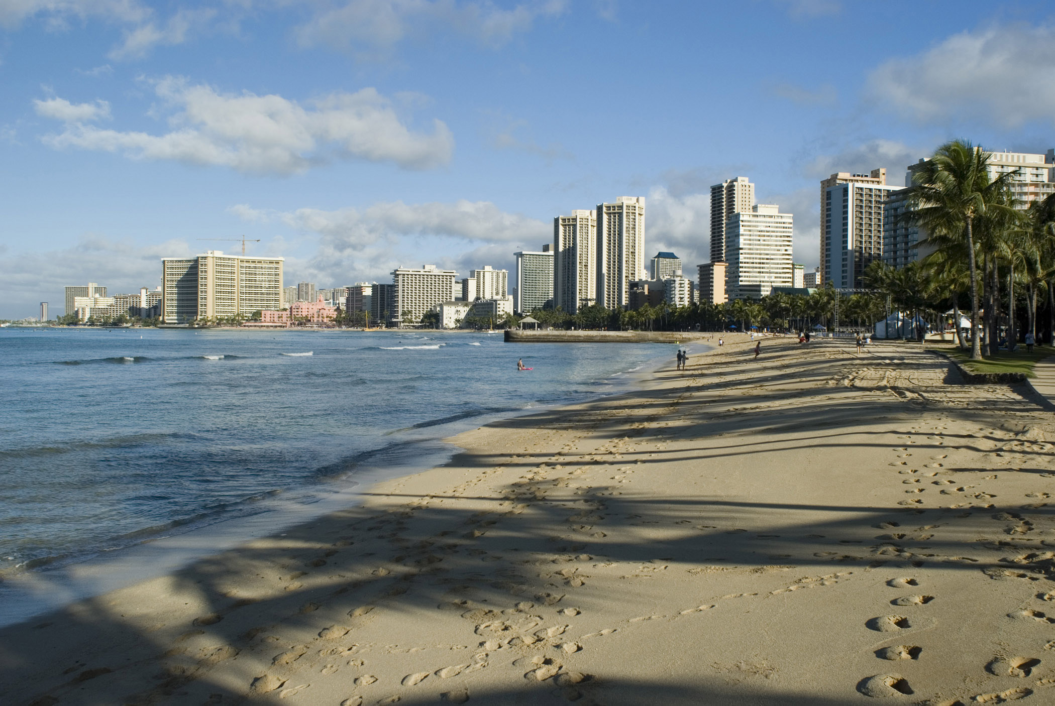 an image of Scenic view of the waterfront and city skyline with footsteps across the golden sand of Waikiki beach, Honolulu, Hawaii