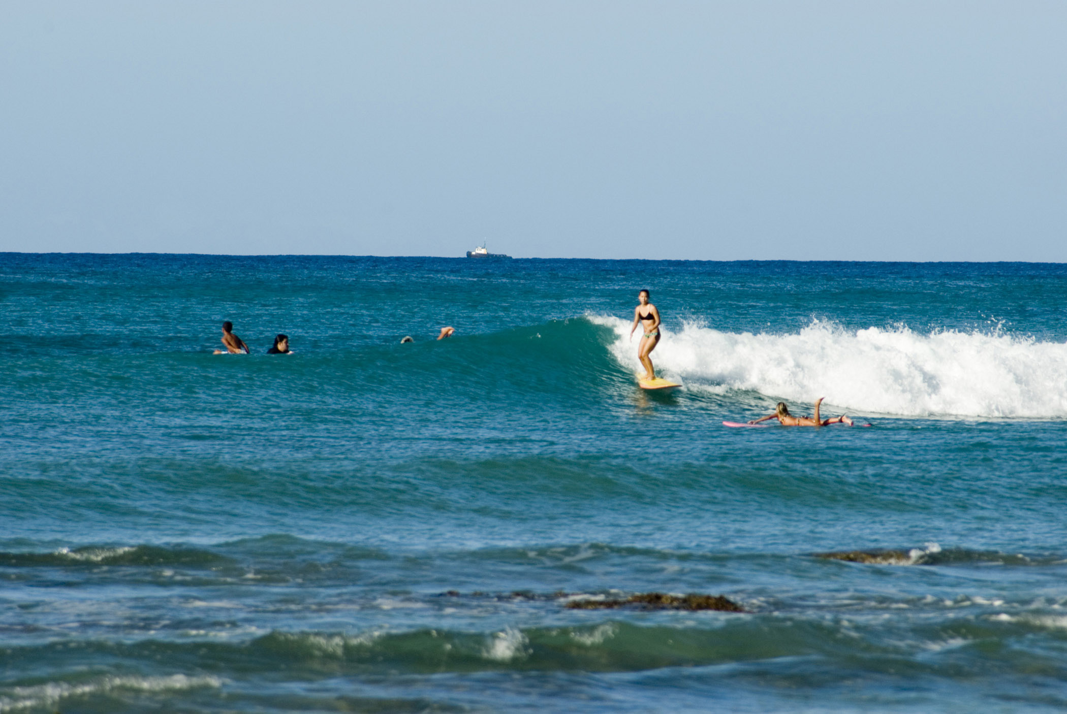 an image of Woman surfing on Waikiki Beach riding in on a wave with other surfers paddling around her, Oahu Island, Hawaii, USA