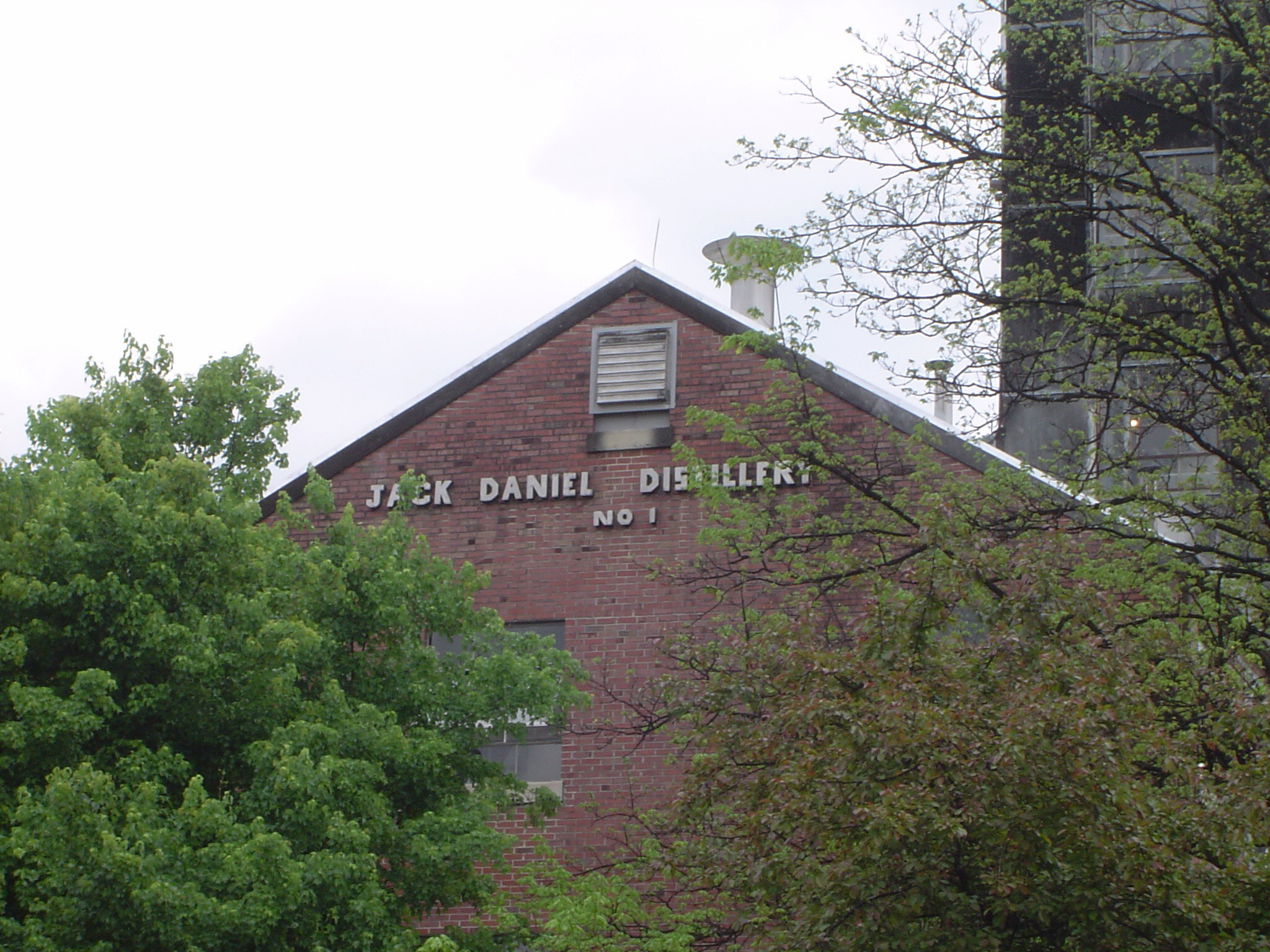 an image of View through green foliage of the external wall and sign for the Jack Daniel Distillery, USA