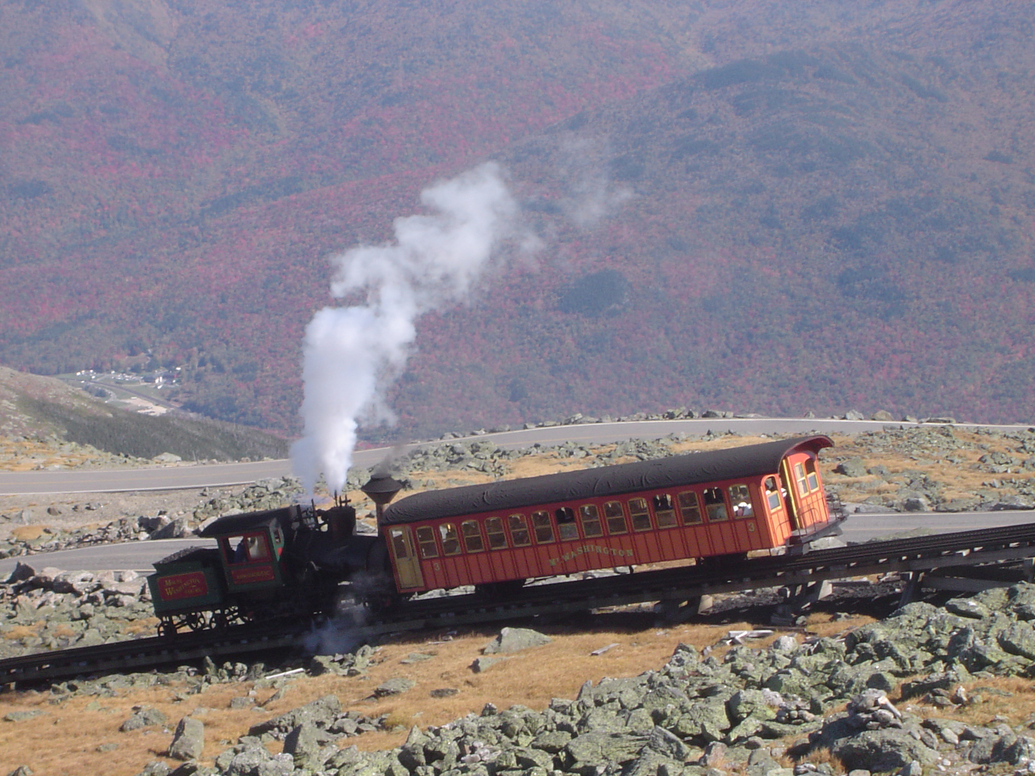 an image of Vintage Steam Locomotive Passing Cog Railway on Rocky Landscape. Captured with Mountains Background.