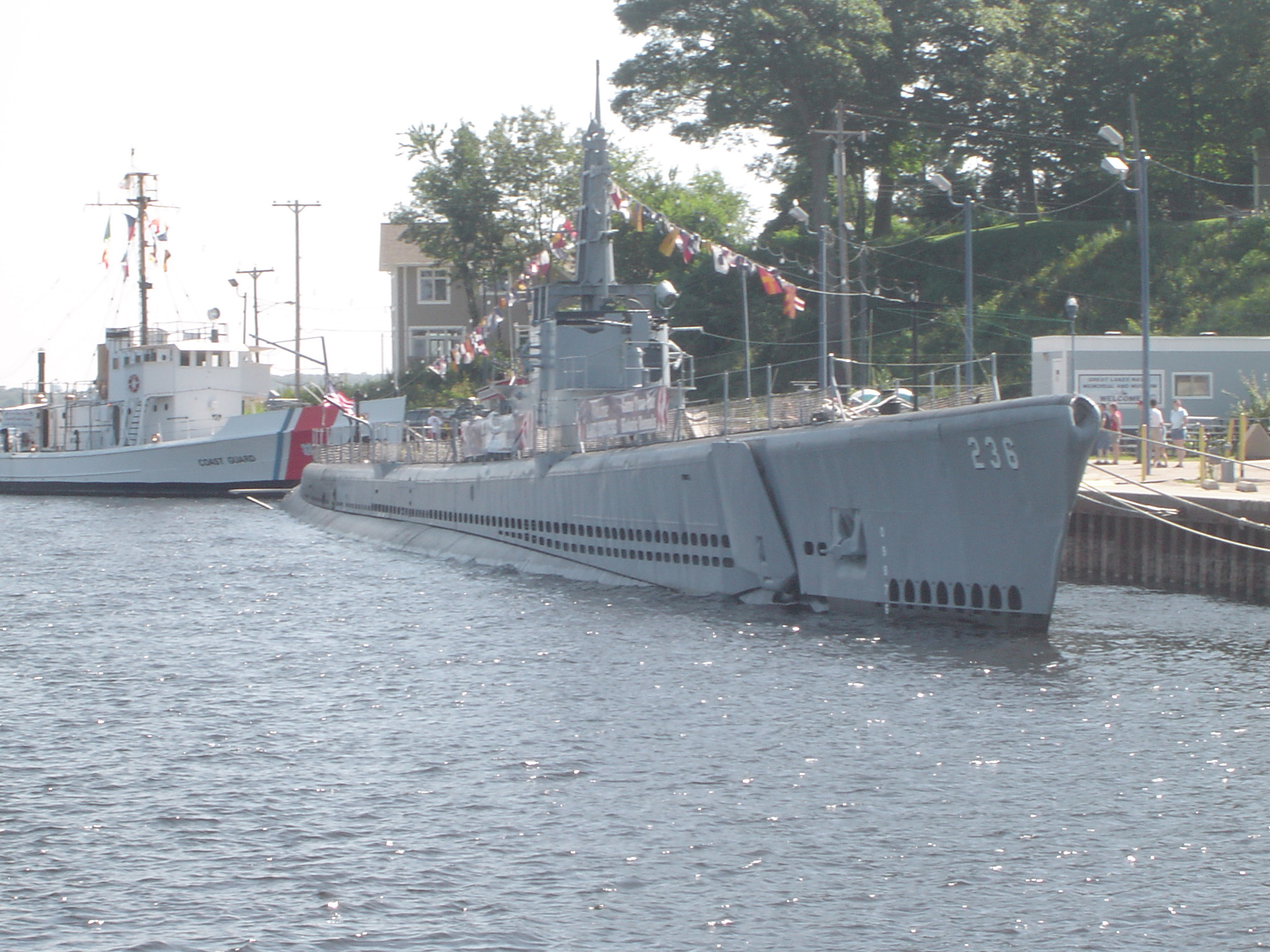 an image of Historical US navy submarine moored on the surface at a dock under colorful bunting
