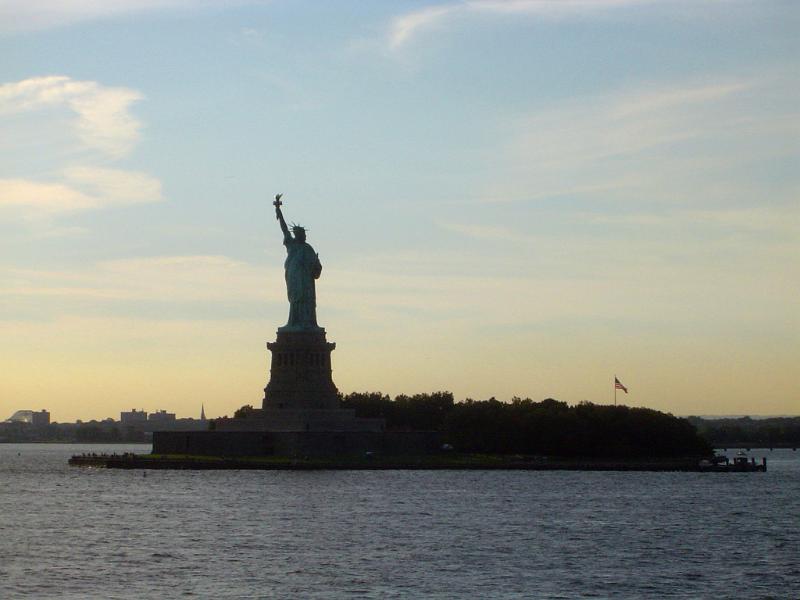 Statue of Liberty, New York , USA, at dusk silhouetted against a colorful evening sky viewed over the water