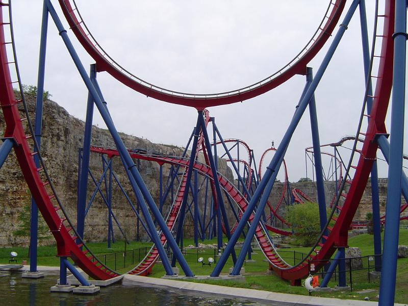 Curves of Roller Coaster Ride on Grassy Land with Concrete Vintage Structure at the Back. Captured on Very Light Blue Gray Sky Background.