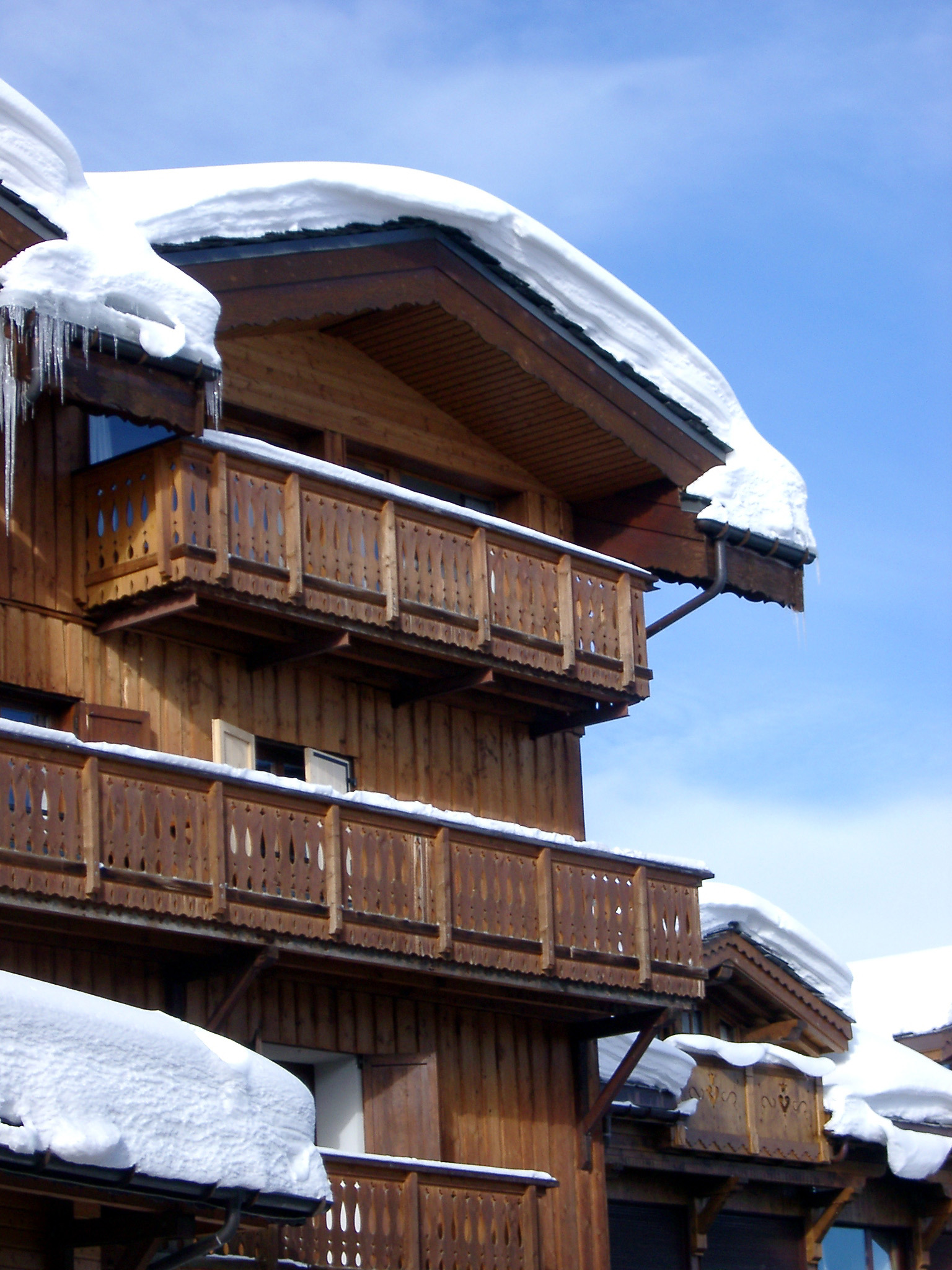 an image of Snow Covering Rooftop of Vintage Wooden Alpine Lodge on Lighter Blue Sky Background.