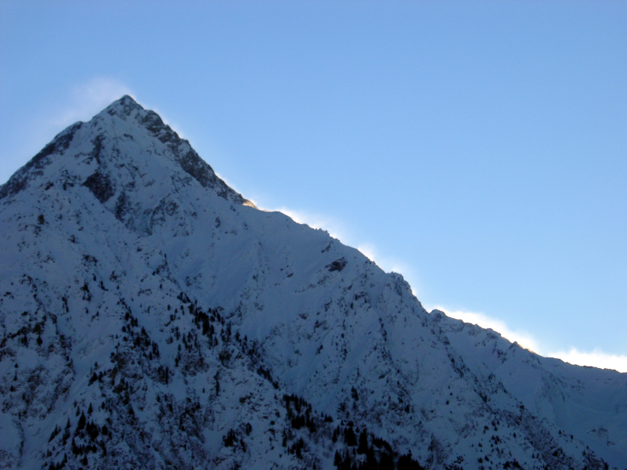 an image of Sunrise of a snow covered mountain peak gilding the rim with a golden glow against a clear blue winter sky