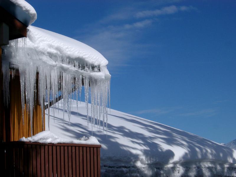 Winter holiday cabin in the Alps with a row of icicles hanging from the roof on a sunny blue sky winter day
