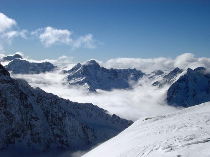 Snow covered mountain peaks in France capped with fluffy white clouds against a clear crisp blue winter sky