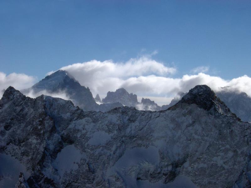 Alpine winter holiday with a view over rugged snow covered mountain ranges and peaks with fluffy white cloud cover under a clear blue sunny sky