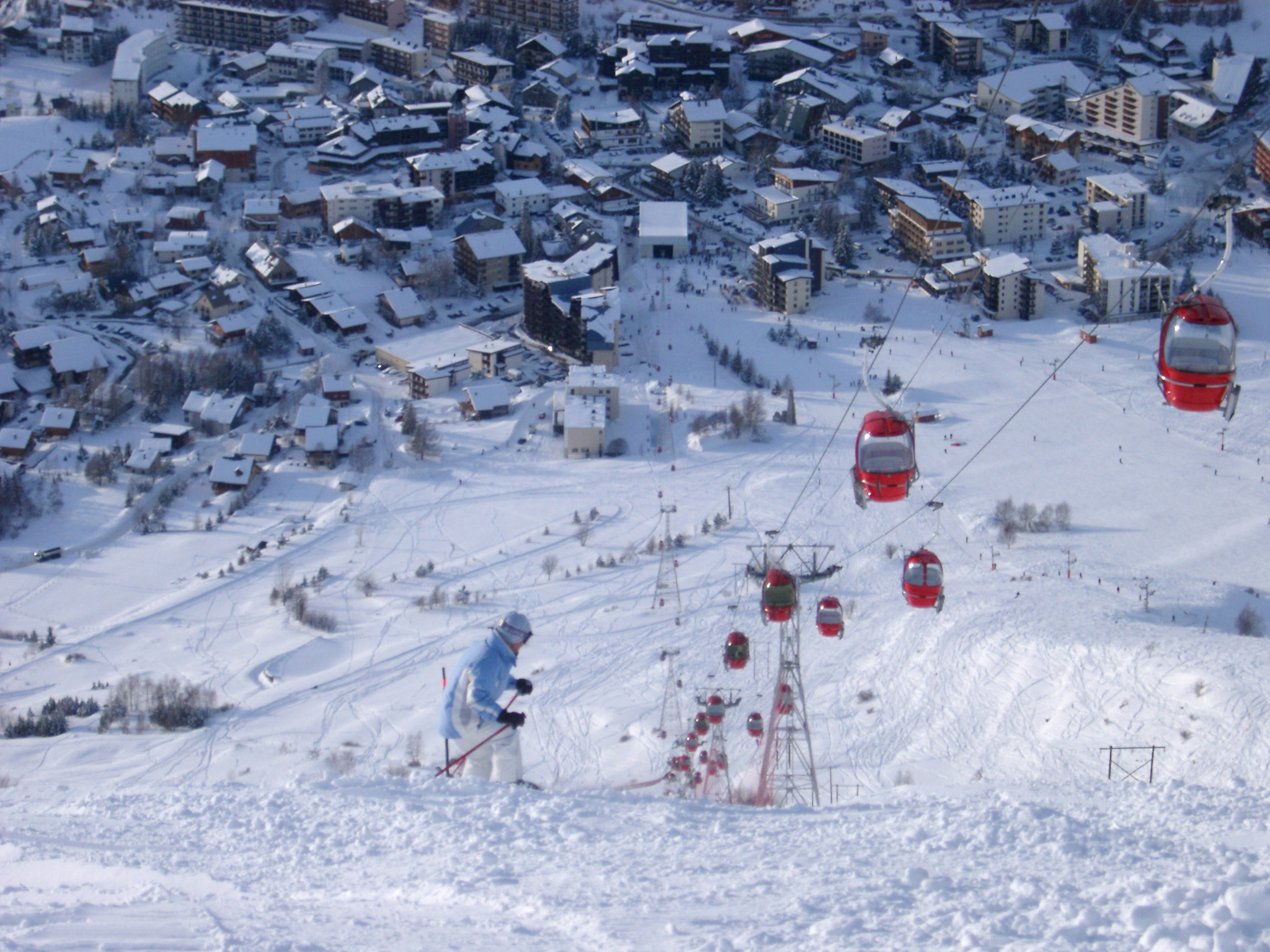 an image of View looking down the piste of a chair lift and snowy alpine village or resort with skiers in winter