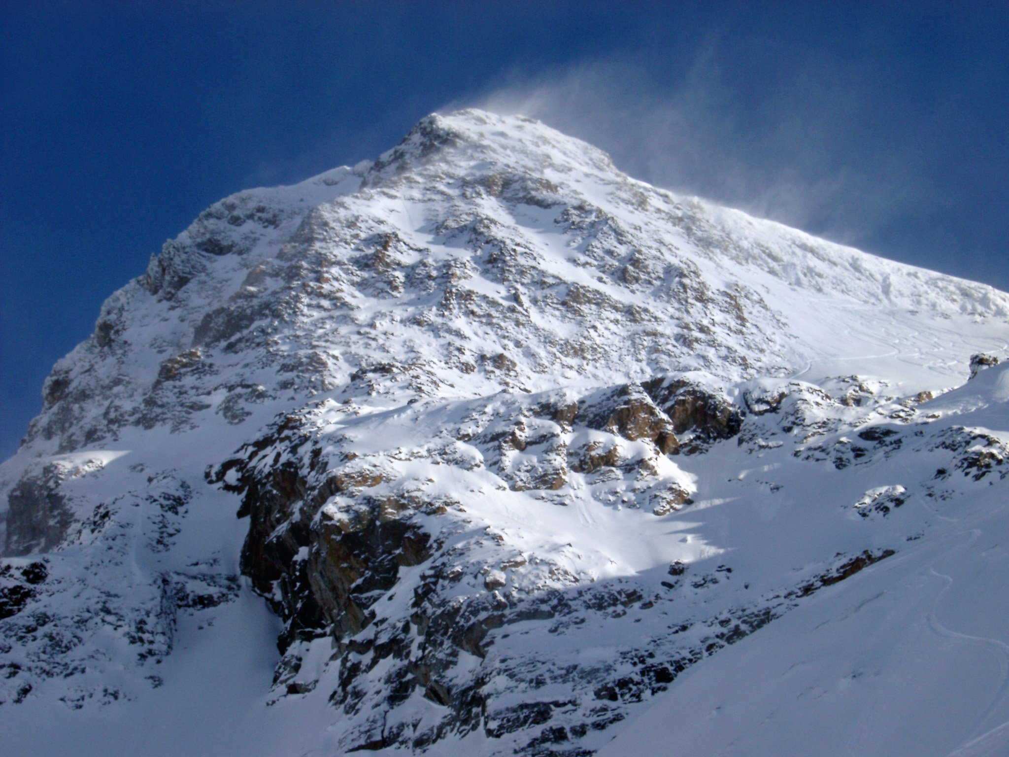 an image of Wind Blown Snow on High Mountain with Blue Sky Background During Winter Holiday.